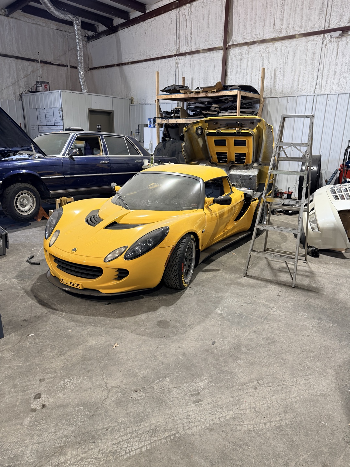 yellow lotus sitting in the shop with back hatch open showing the engine and transmission